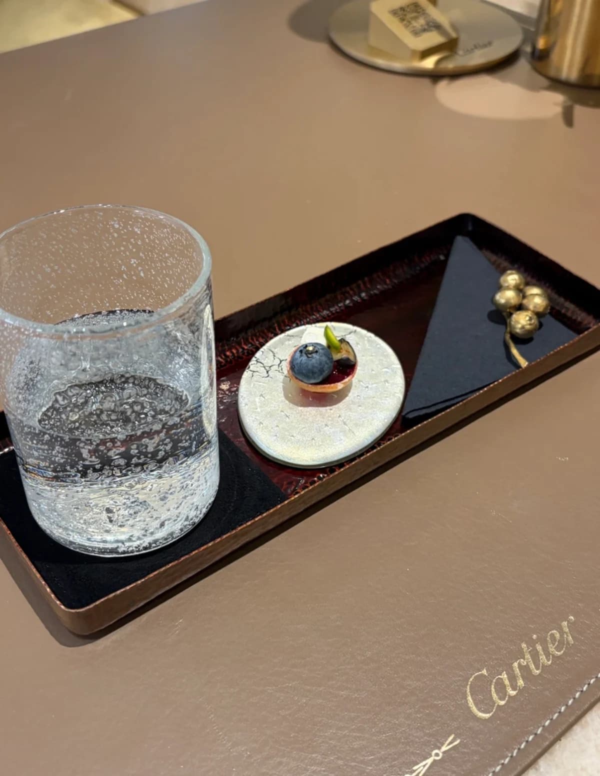 Welcome dessert and a glass of sparkling water on a lacquered tray at the Cartier Maison