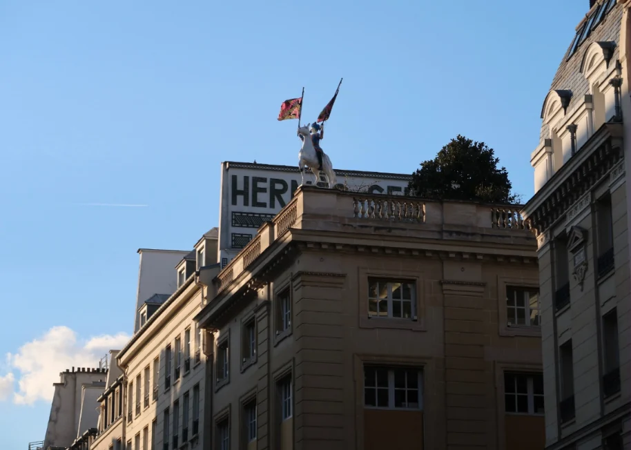 Horseman statue holding two scarf flags on the rooftop of the Hermès building at 24 Rue du Faubourg-Saint-Honoré, Paris, against a blue sky