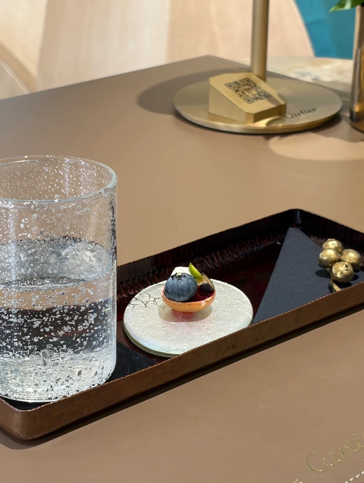 Close view of the welcome dessert on a small ceramic plate beside a textured glass of water at the Cartier Maison