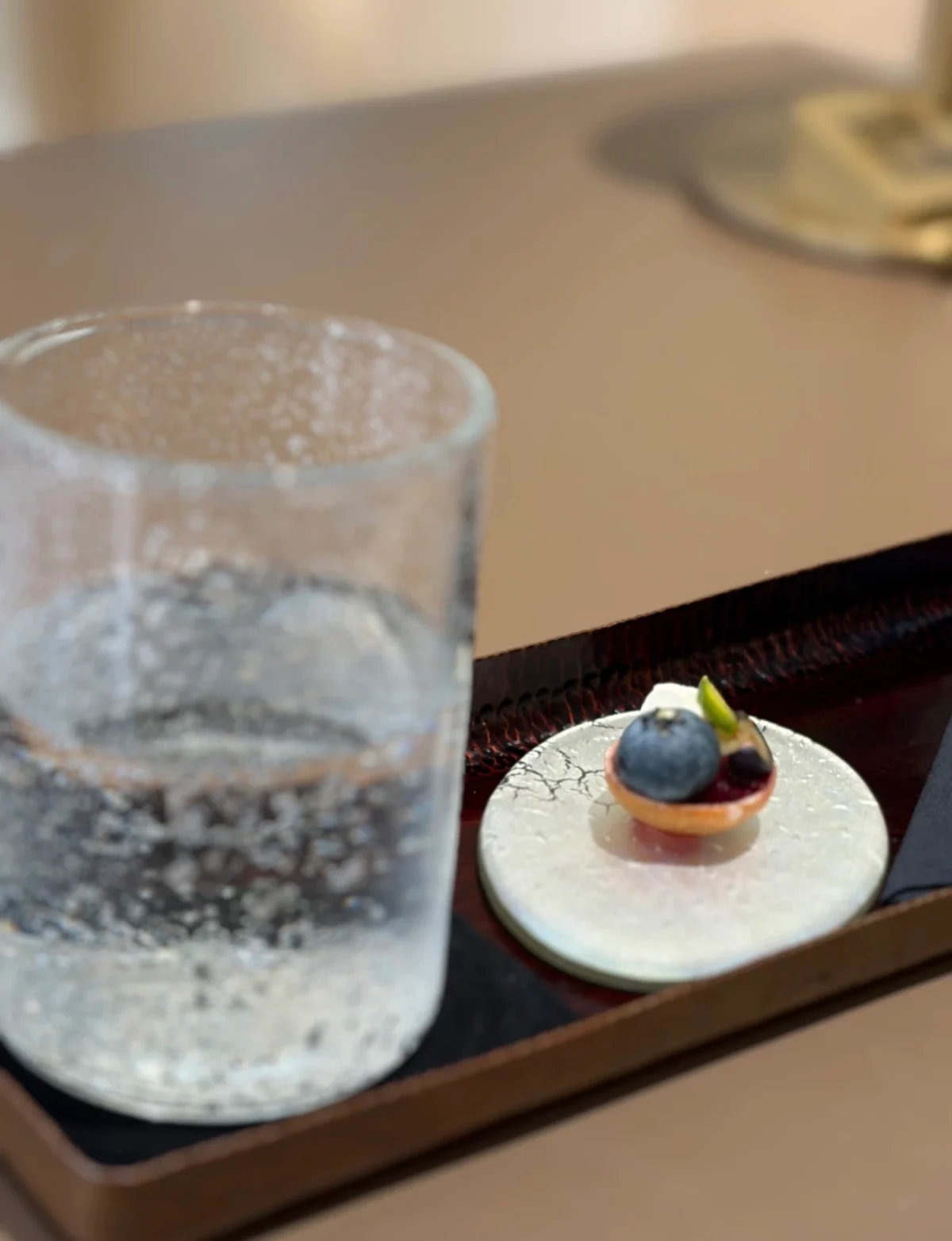 Textured handmade glass and a small dessert plate on a dark tray at the Cartier Maison